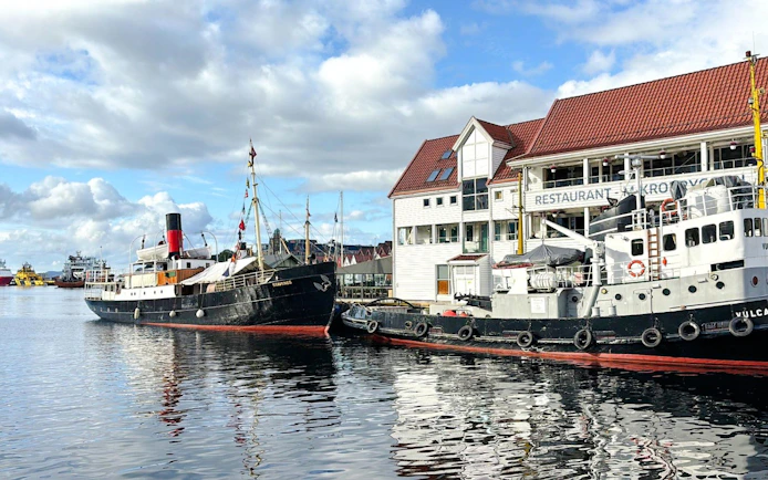 Historic ships docked at Bergen Pier, Norway, with waterfront buildings in the background.