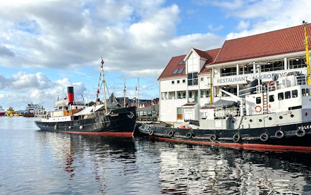 Historic ships docked at Bergen Pier, Norway, with waterfront buildings in the background.
