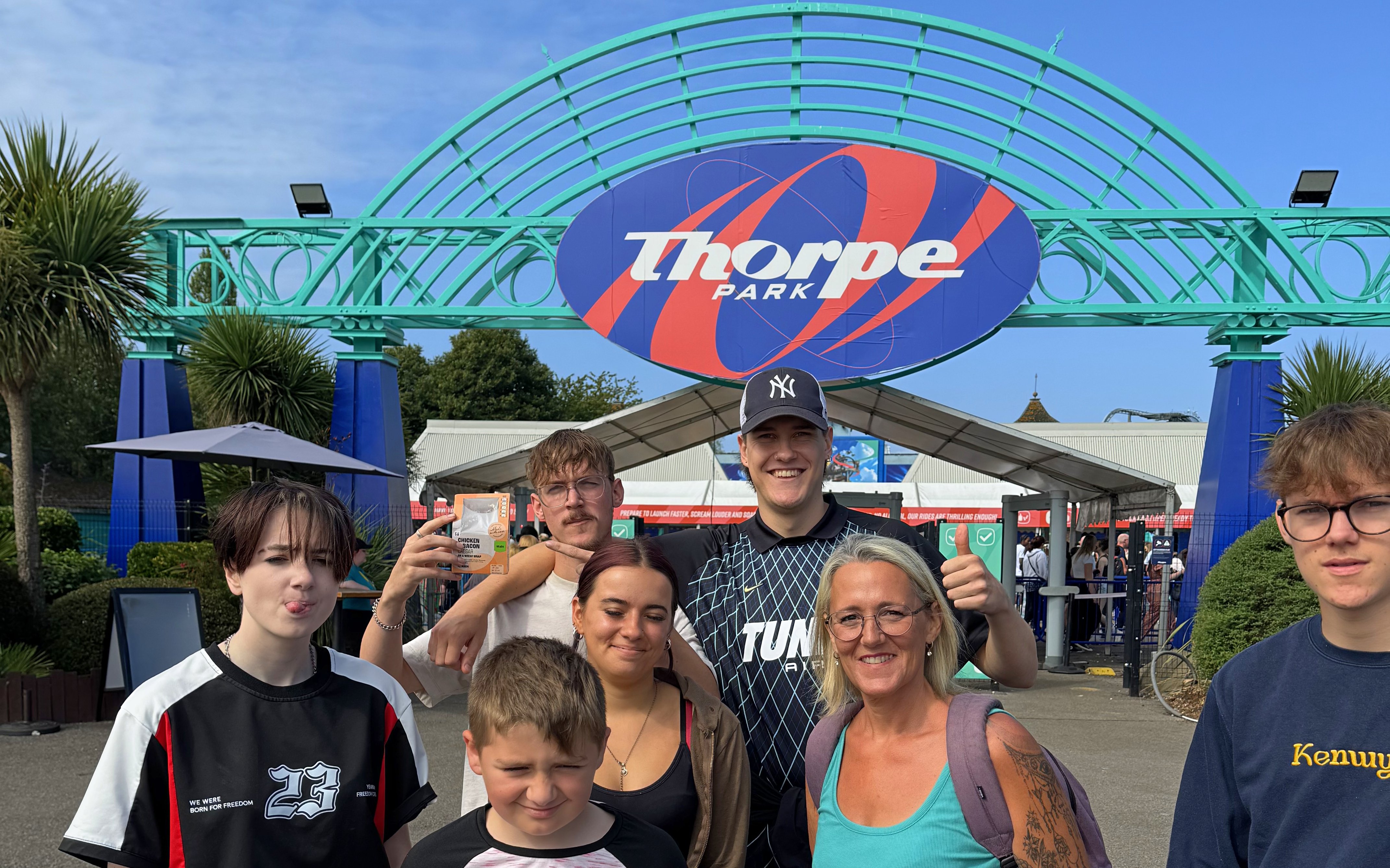Group of people at Thorpe Park entrance with park sign in background.