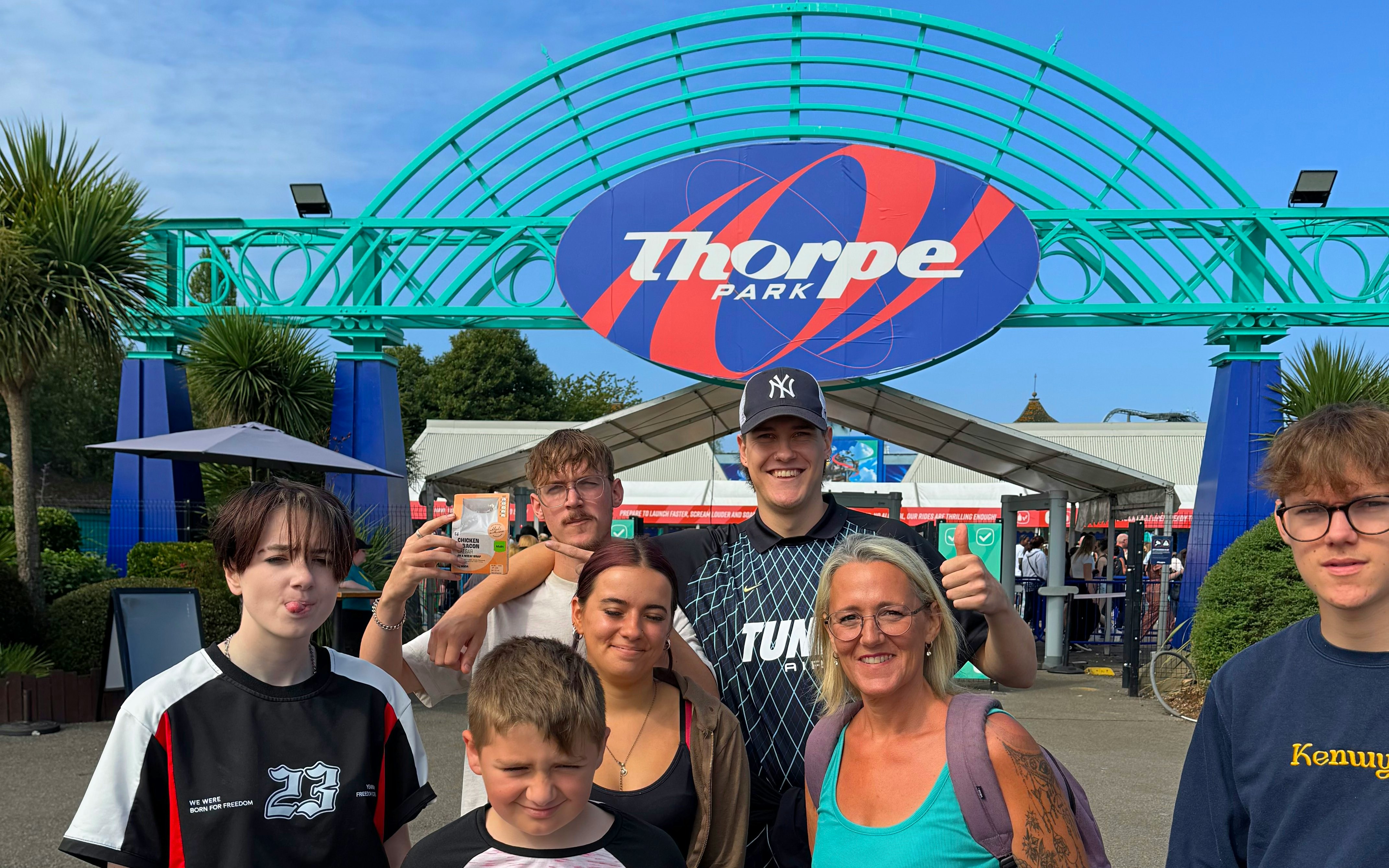 Group of people at Thorpe Park entrance with park sign in background.