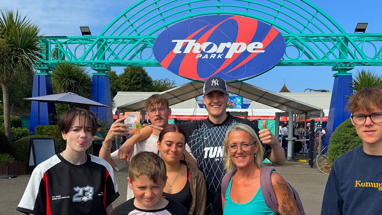 Group of people at Thorpe Park entrance with park sign in background.