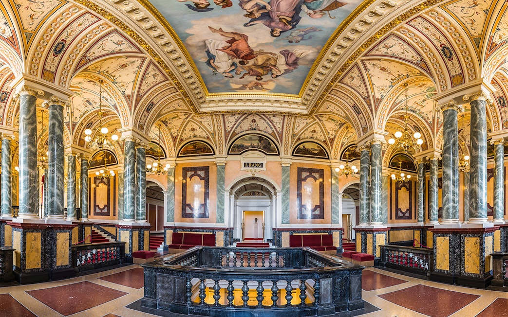 Ornate interior of the Semperoper in Dresden with marble columns and detailed ceiling frescoes.