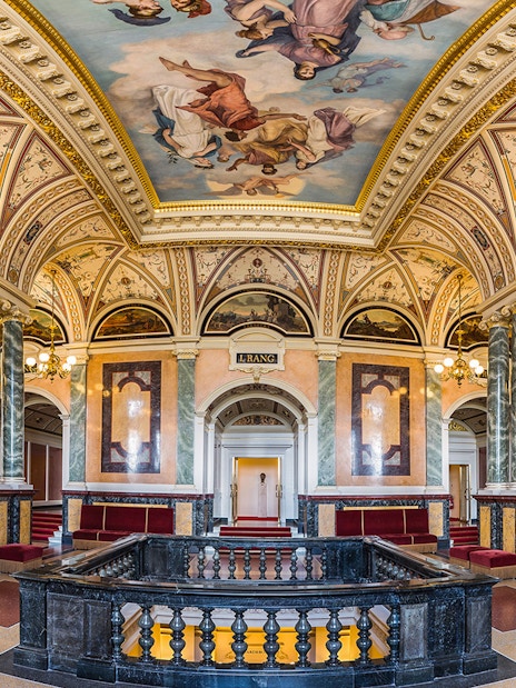 Ornate interior of the Semperoper in Dresden with marble columns and detailed ceiling frescoes.