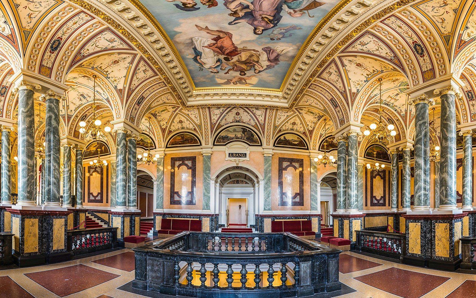 Ornate interior of the Semperoper in Dresden with marble columns and detailed ceiling frescoes.