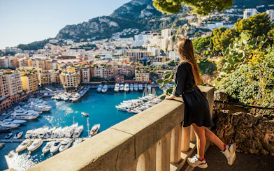 Woman overlooking Monaco harbor with yachts and cityscape from a viewpoint.