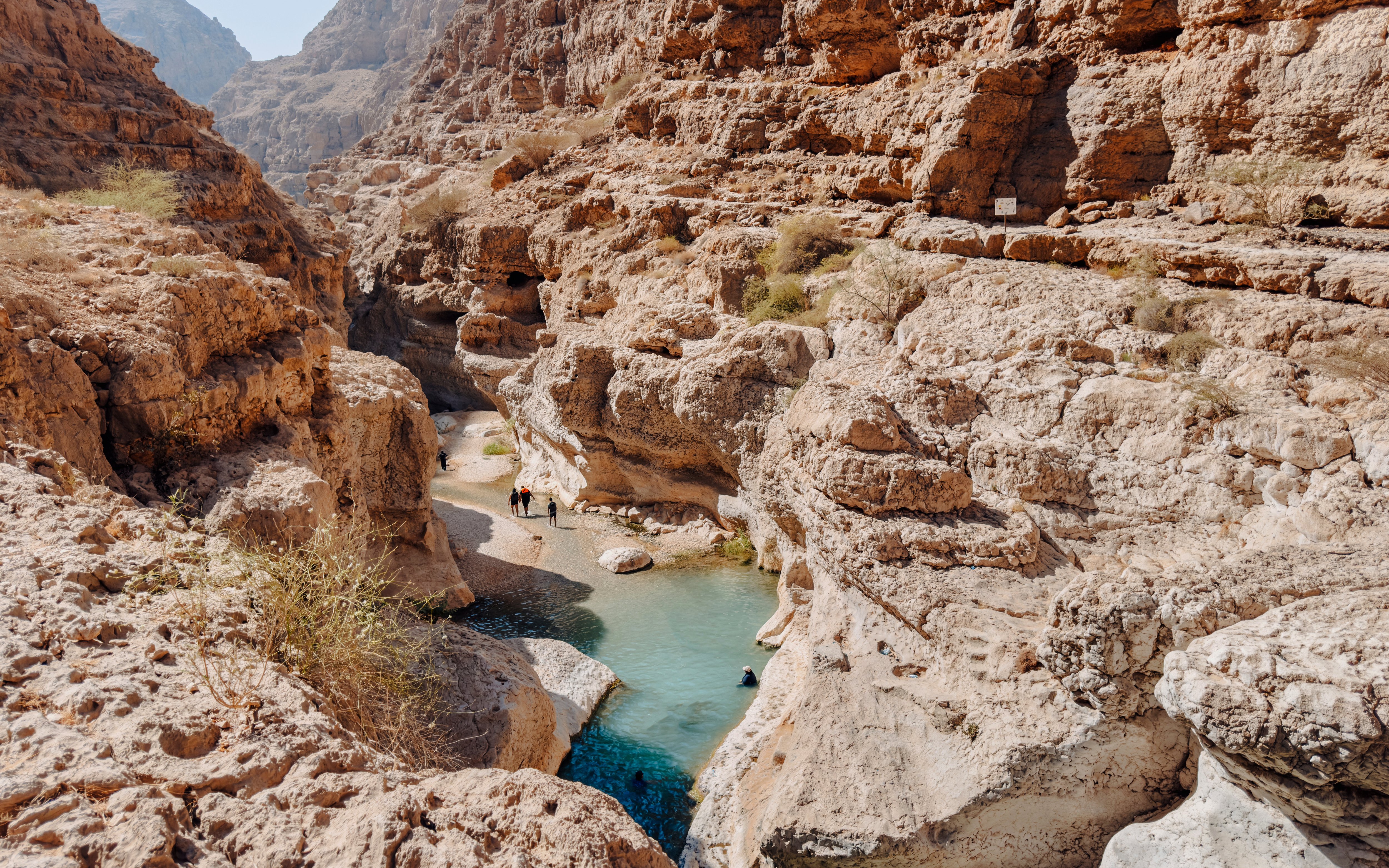 Hikers exploring rocky canyon and turquoise pools in Wadi Shab, Oman.