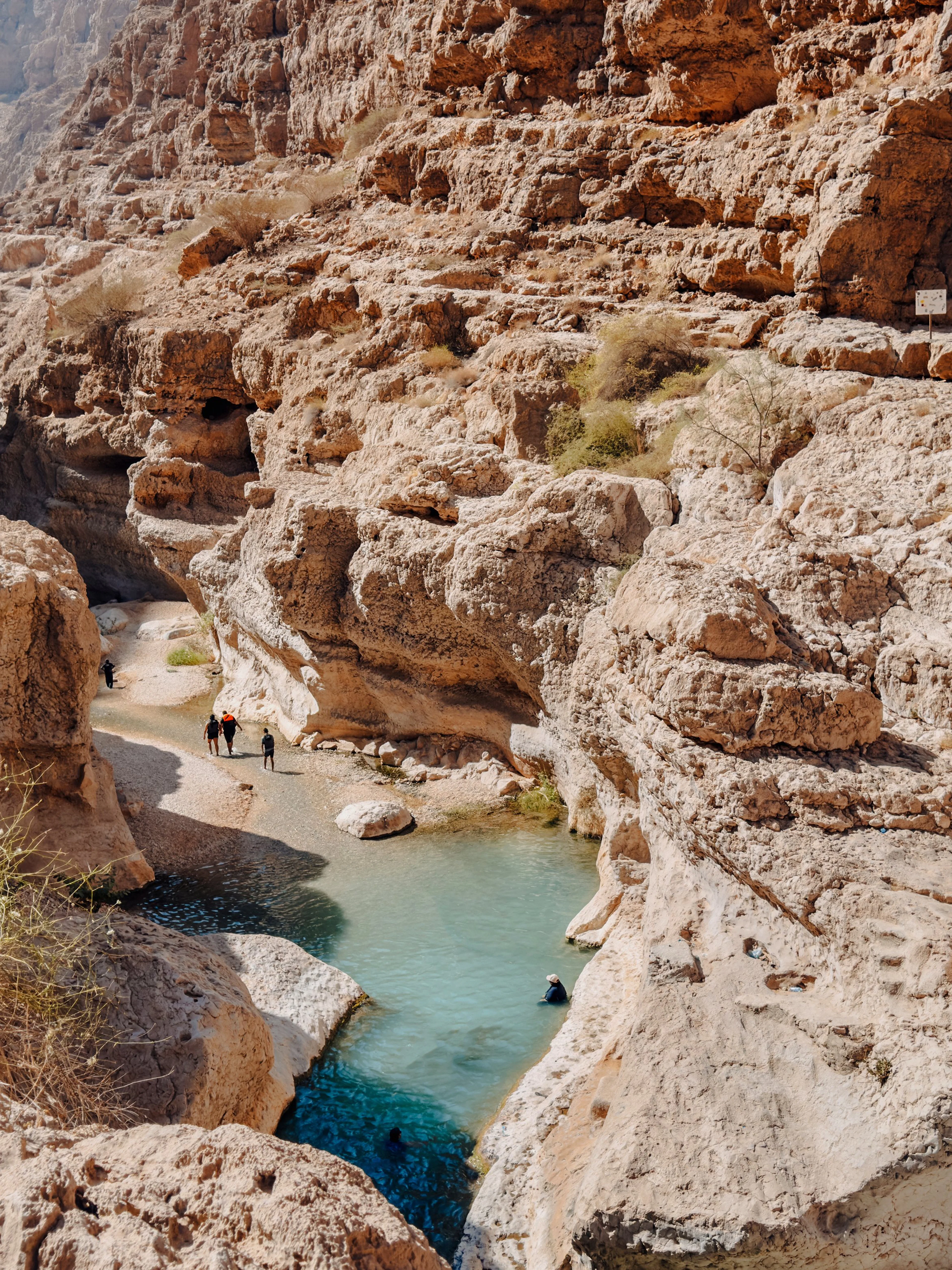 Hikers exploring rocky canyon and turquoise pools in Wadi Shab, Oman.