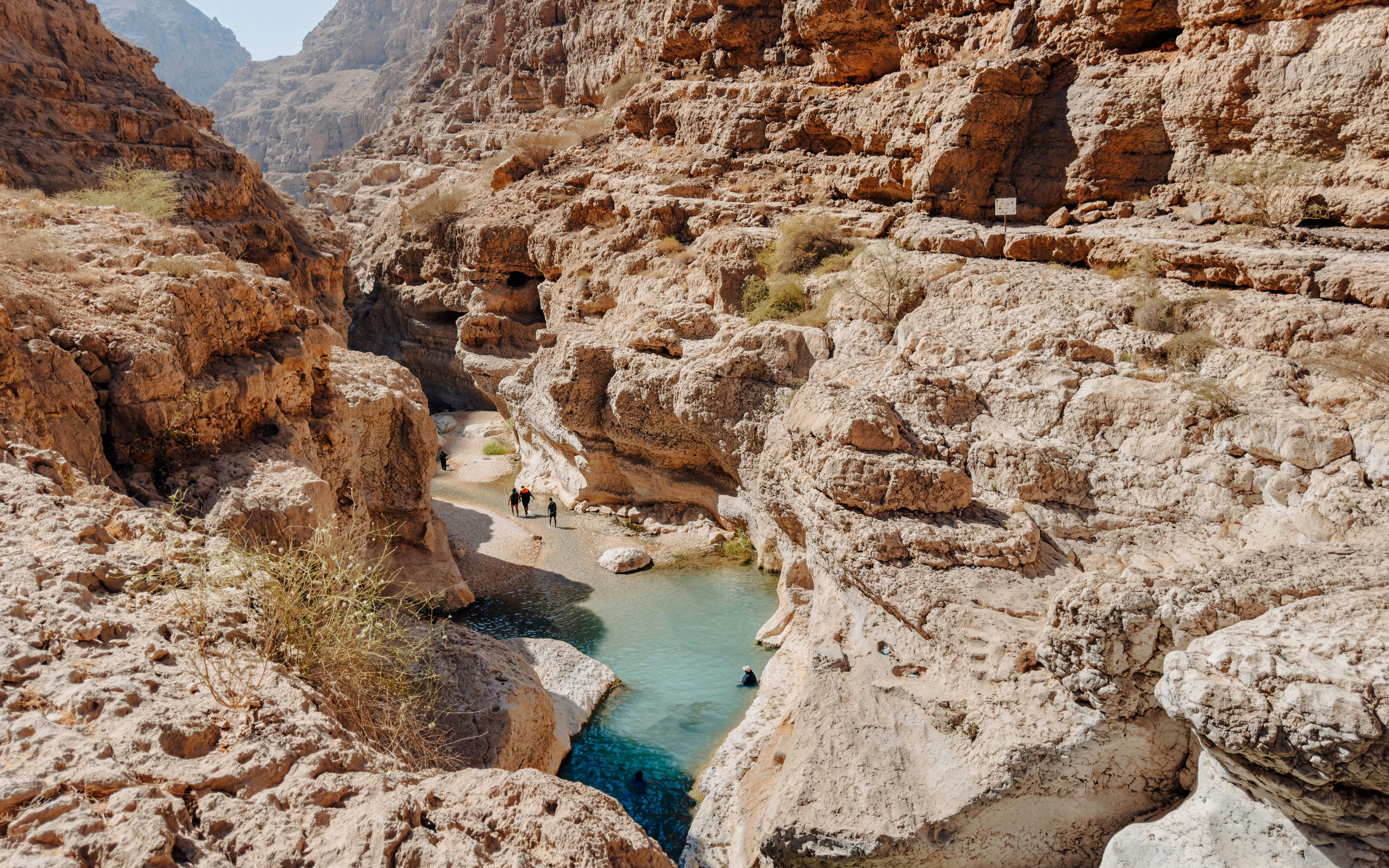 Hikers exploring rocky canyon and turquoise pools in Wadi Shab, Oman.