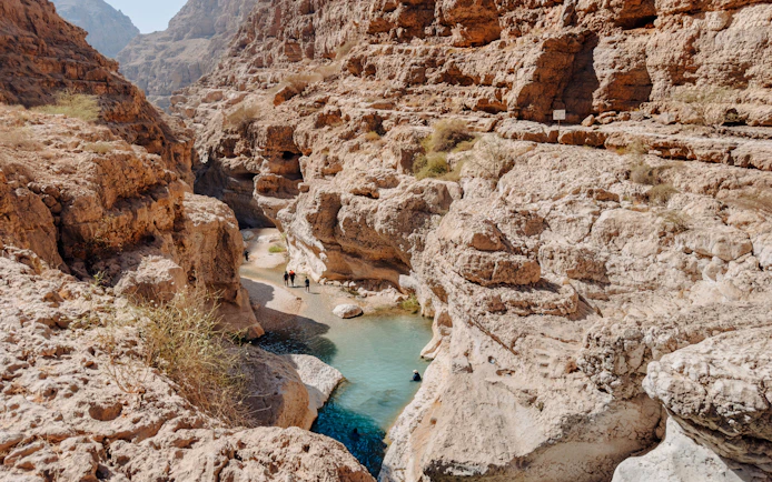 Hikers exploring rocky canyon and turquoise pools in Wadi Shab, Oman.