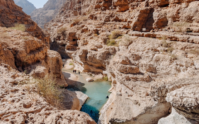 Hikers exploring rocky canyon and turquoise pools in Wadi Shab, Oman.