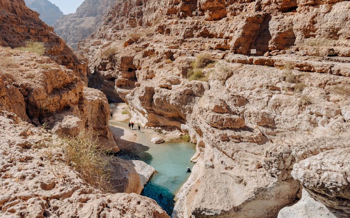 Hikers exploring rocky canyon and turquoise pools in Wadi Shab, Oman.