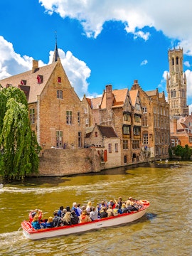 Boat tour on a canal in Bruges with the Belfry tower in the background.