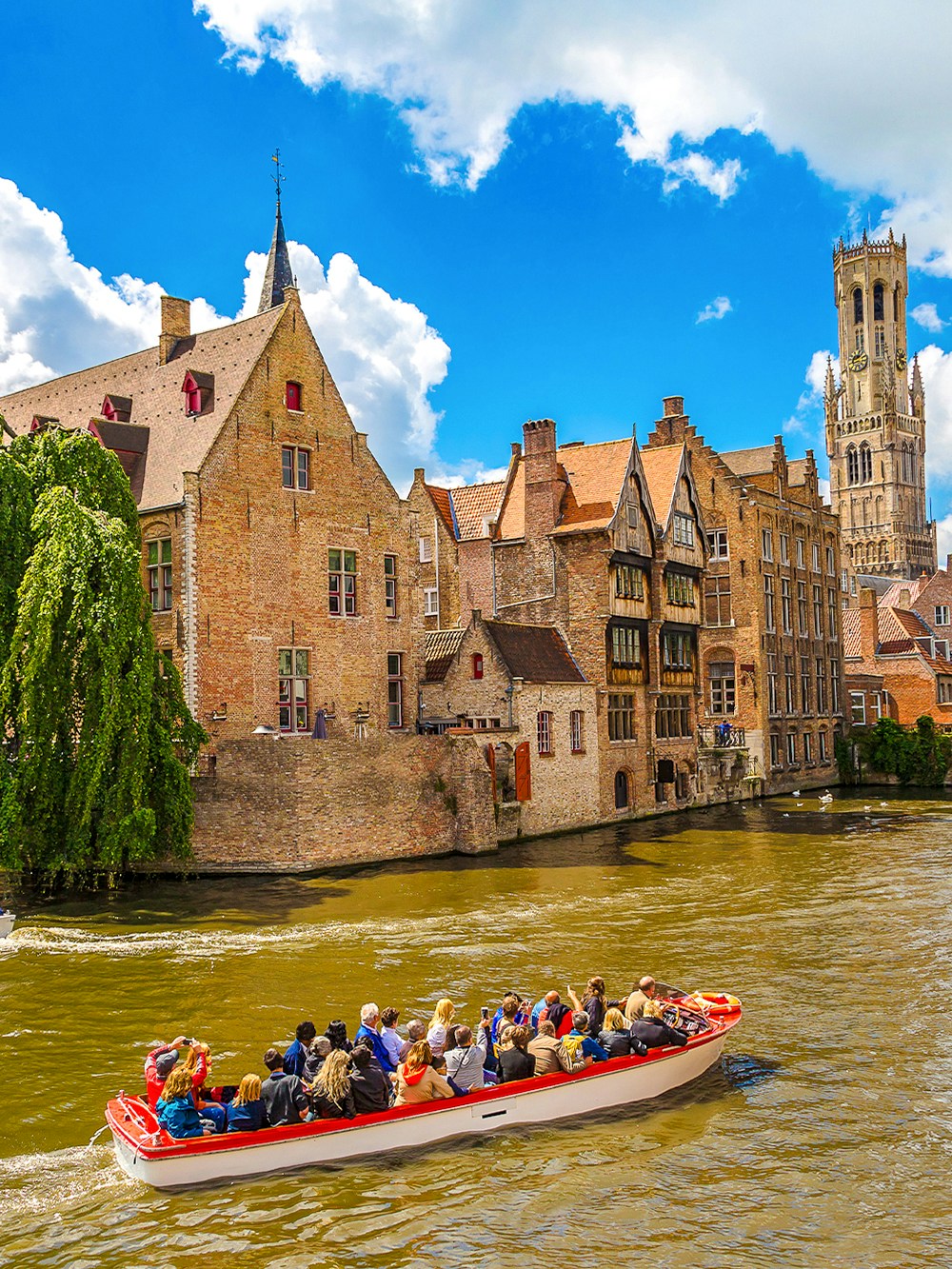 Boat tour on a canal in Bruges with the Belfry tower in the background.