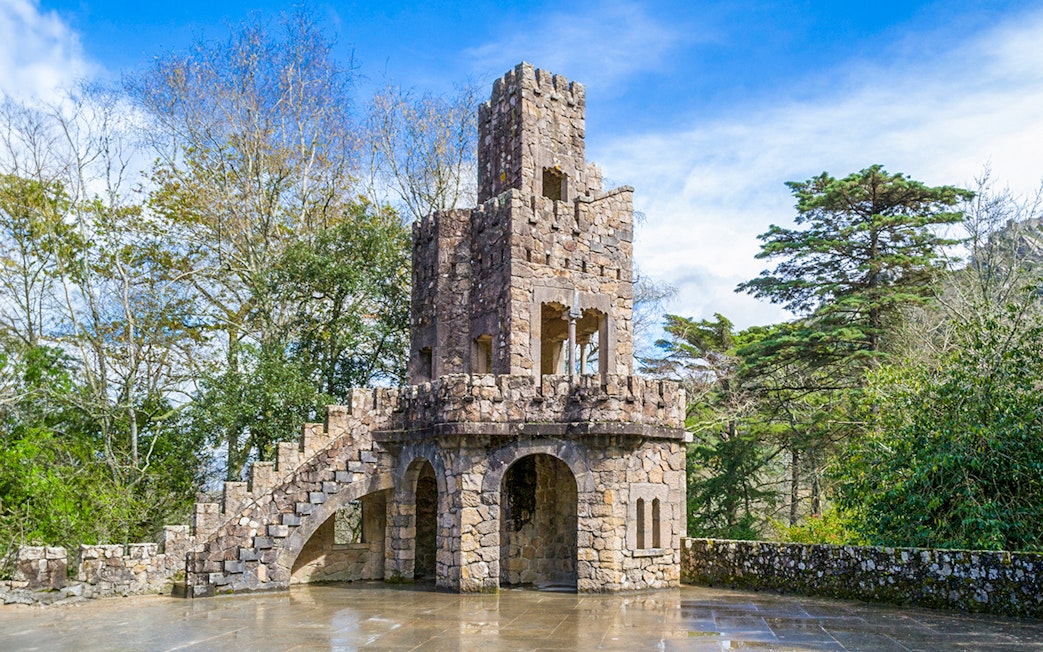 Stone tower at Quinta da Regaleira, Sintra, surrounded by trees.