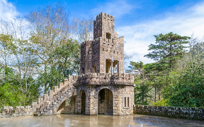 Stone tower at Quinta da Regaleira, Sintra, surrounded by trees.