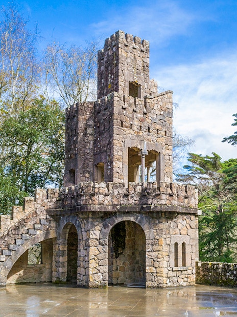 Stone tower at Quinta da Regaleira, Sintra, surrounded by trees.