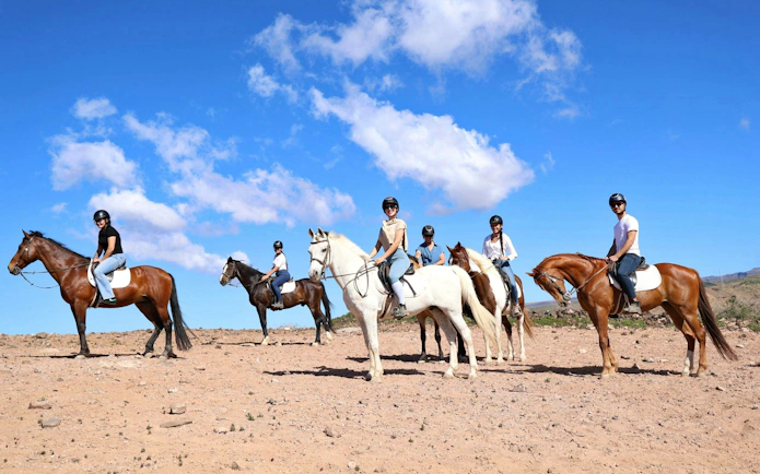 Horse riders on a volcanic trail in Gran Canaria under a clear blue sky.