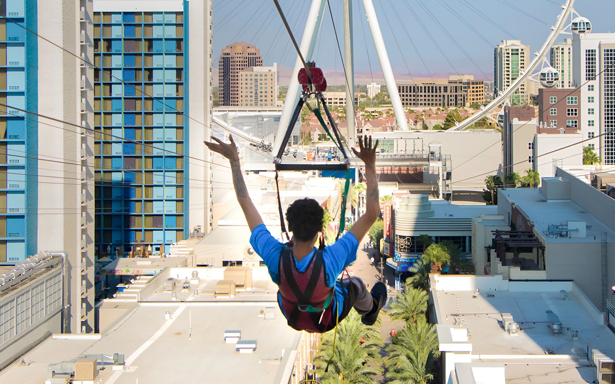 Person ziplining over Las Vegas with cityscape and High Roller observation wheel in view.