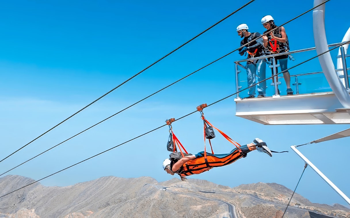 Person ziplining on Jais Flight in Jebel Jais mountains, others watching from platform.