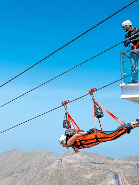 Person ziplining on Jais Flight in Jebel Jais mountains, others watching from platform.