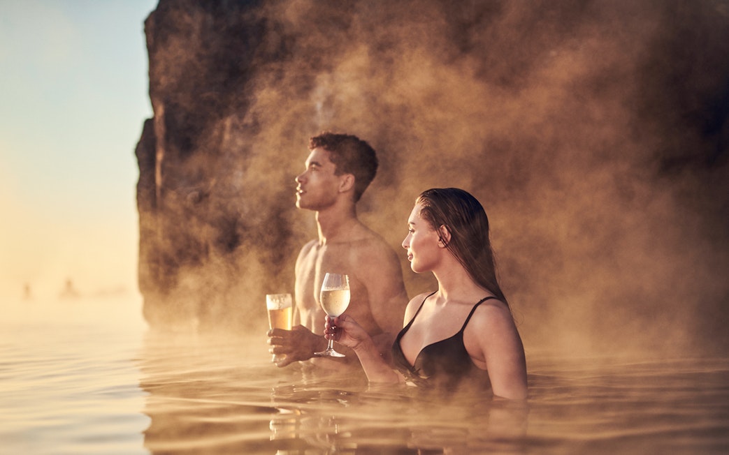 Couple enjoying drinks in the warm waters of Sky Lagoon Saman Pass.
