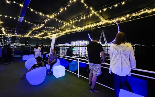 Houseboat deck with people enjoying night view of Ain Dubai Ferris wheel.