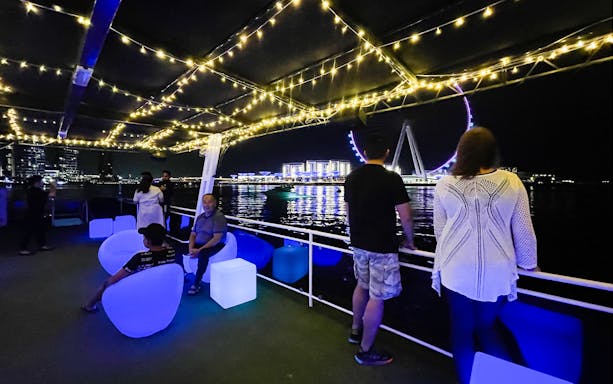 Houseboat deck with people enjoying night view of Ain Dubai Ferris wheel.
