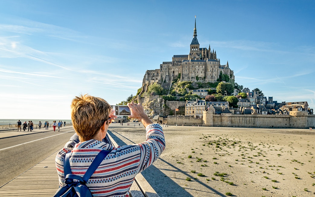 Visitor photographing Mont Saint-Michel with smartphone, France.