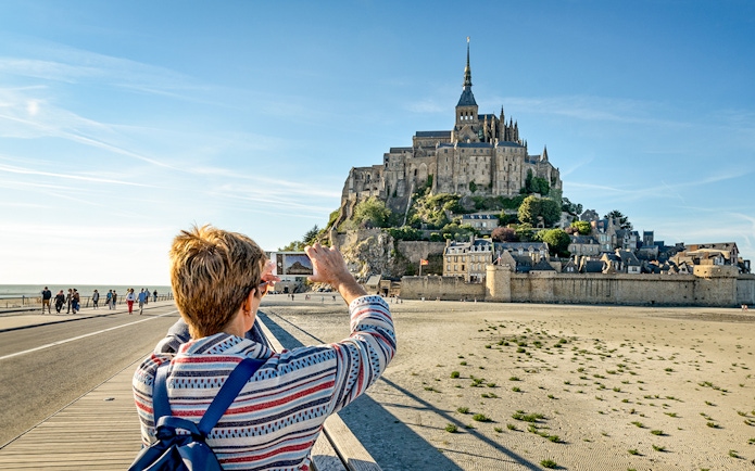 Visitor photographing Mont Saint-Michel with smartphone, France.