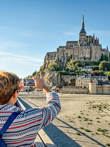 Visitor photographing Mont Saint-Michel with smartphone, France.