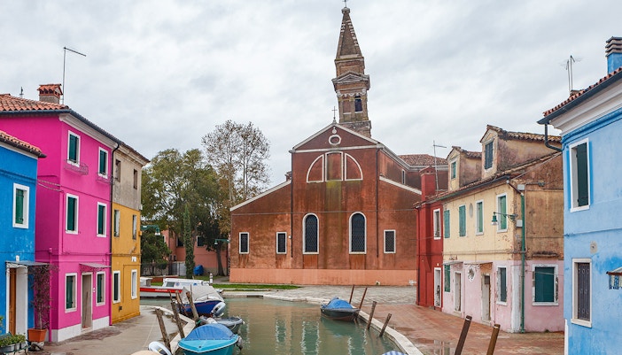 Chiesa di San Martino bell tower in Burano, Italy, with colorful houses in the foreground.
