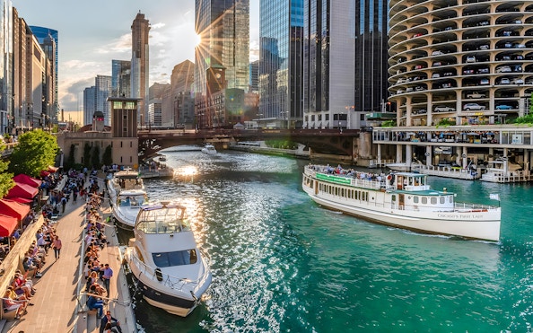 Chicago Riverwalk with people strolling, boats on the river, and 'Chicago's First Lady' tour boat.