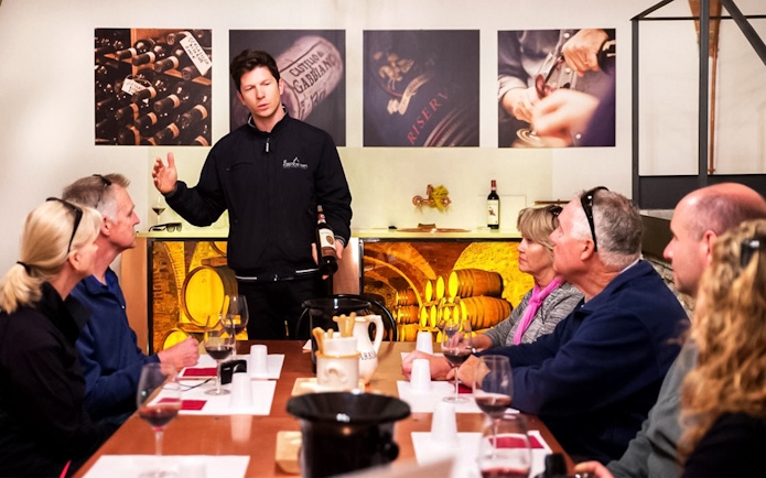 Group enjoying wine tasting session in Chianti with guide explaining wine details.