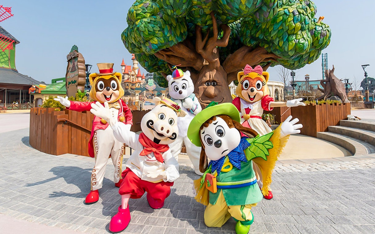 Characters in colorful costumes at Lotte World Adventure, Busan, with a whimsical tree backdrop.