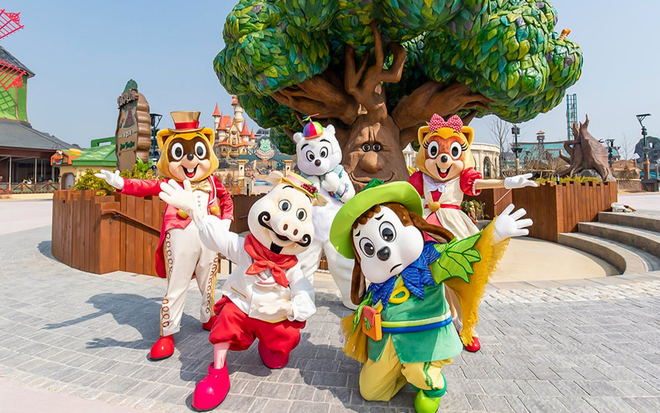 Characters in colorful costumes at Lotte World Adventure, Busan, with a whimsical tree backdrop.
