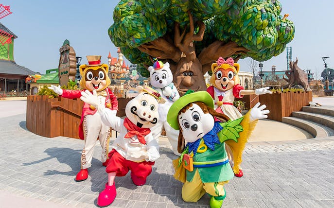 Characters in colorful costumes at Lotte World Adventure, Busan, with a whimsical tree backdrop.