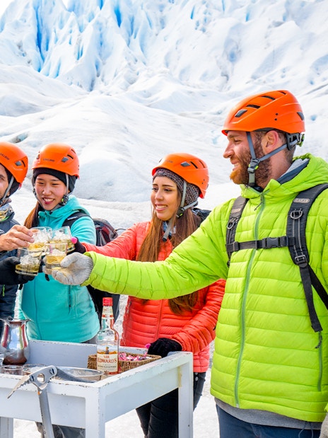 Tourists with guide toasting drinks atop Perito Moreno Glacier, Argentina.