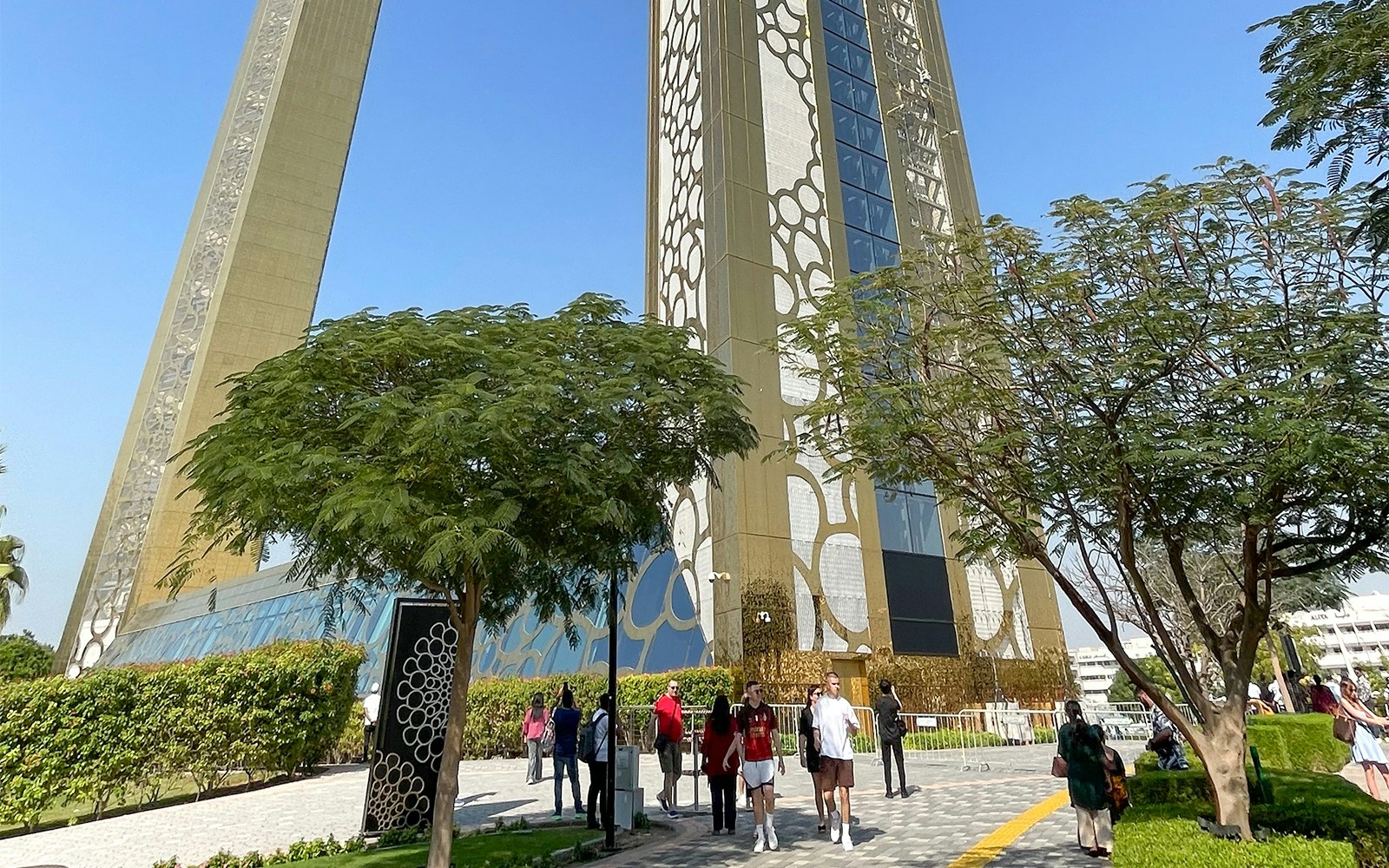 Dubai Frame with visitors walking nearby, surrounded by trees and greenery.