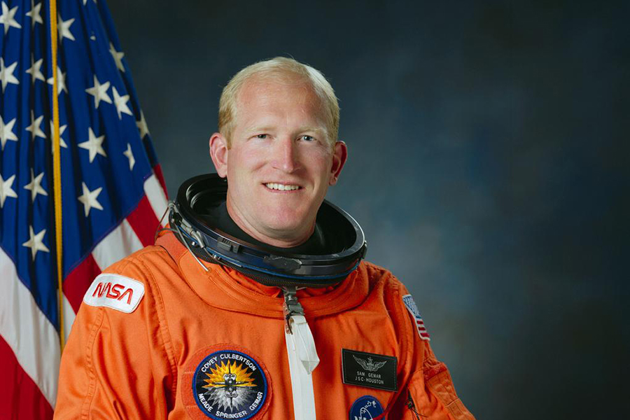 Astronaut Sam Gemar in space suit against a starry backdrop.