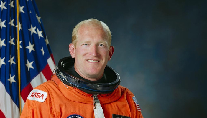 Astronaut Sam Gemar in space suit against a starry backdrop.
