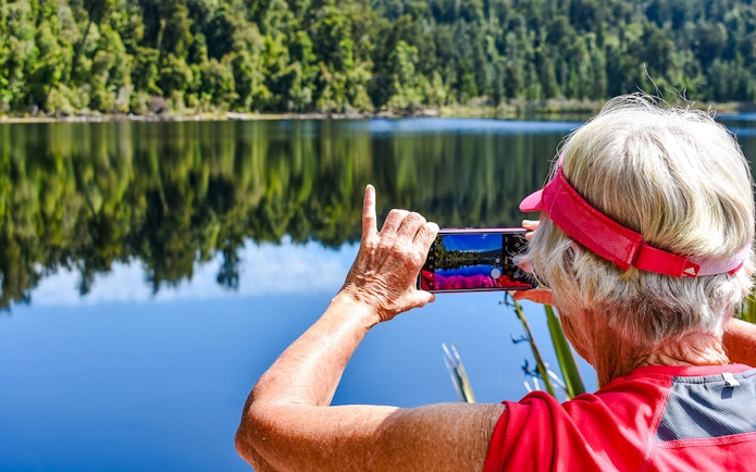 Tourist photographing rainforest reflection at Franz Josef.