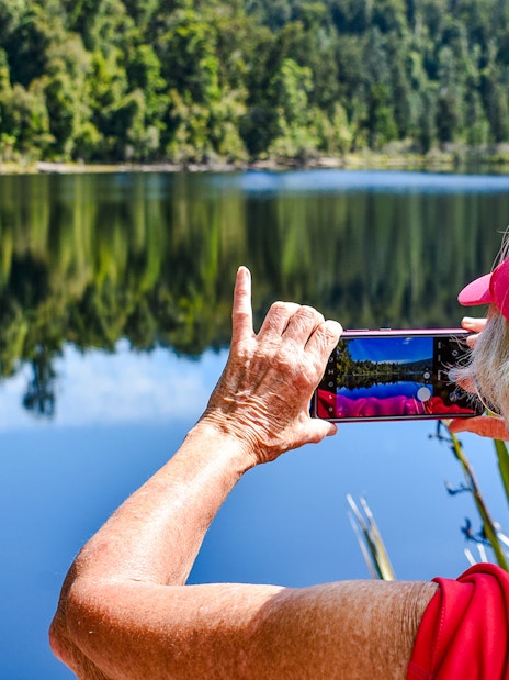 Tourist photographing rainforest reflection at Franz Josef.