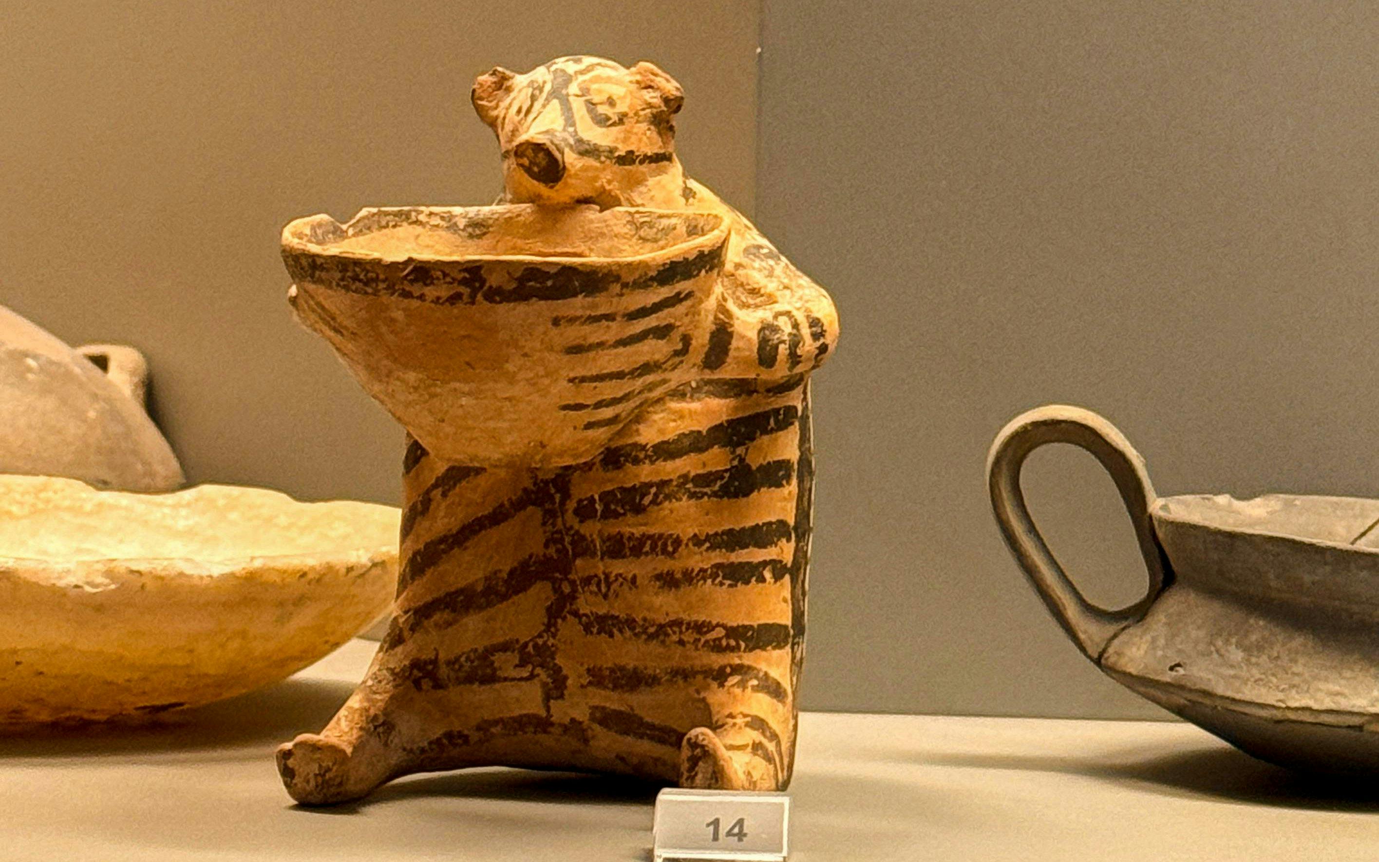 Striped ceramic figurine holding a bowl, National Archaeological Museum, Athens.