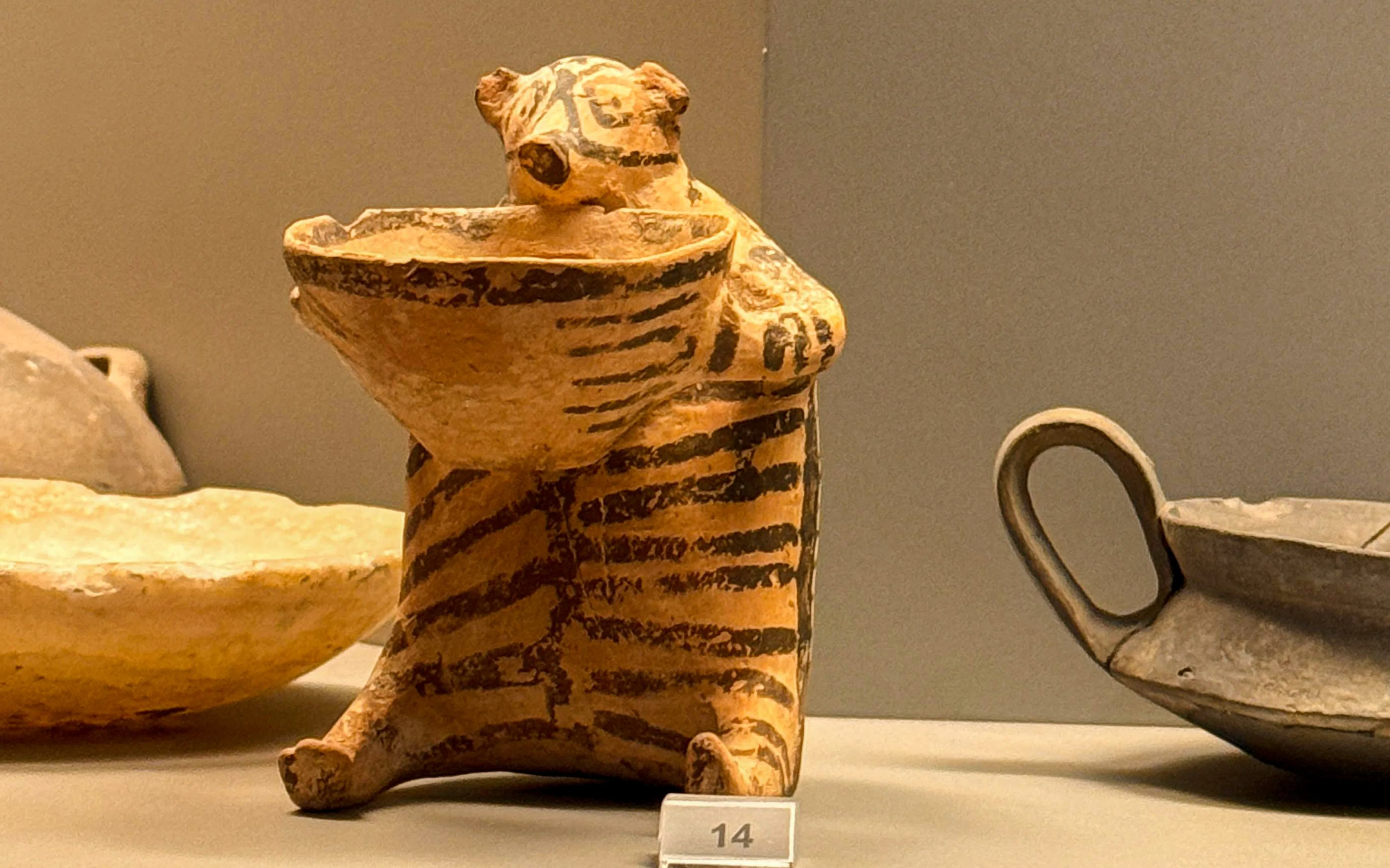 Striped ceramic figurine holding a bowl, National Archaeological Museum, Athens.