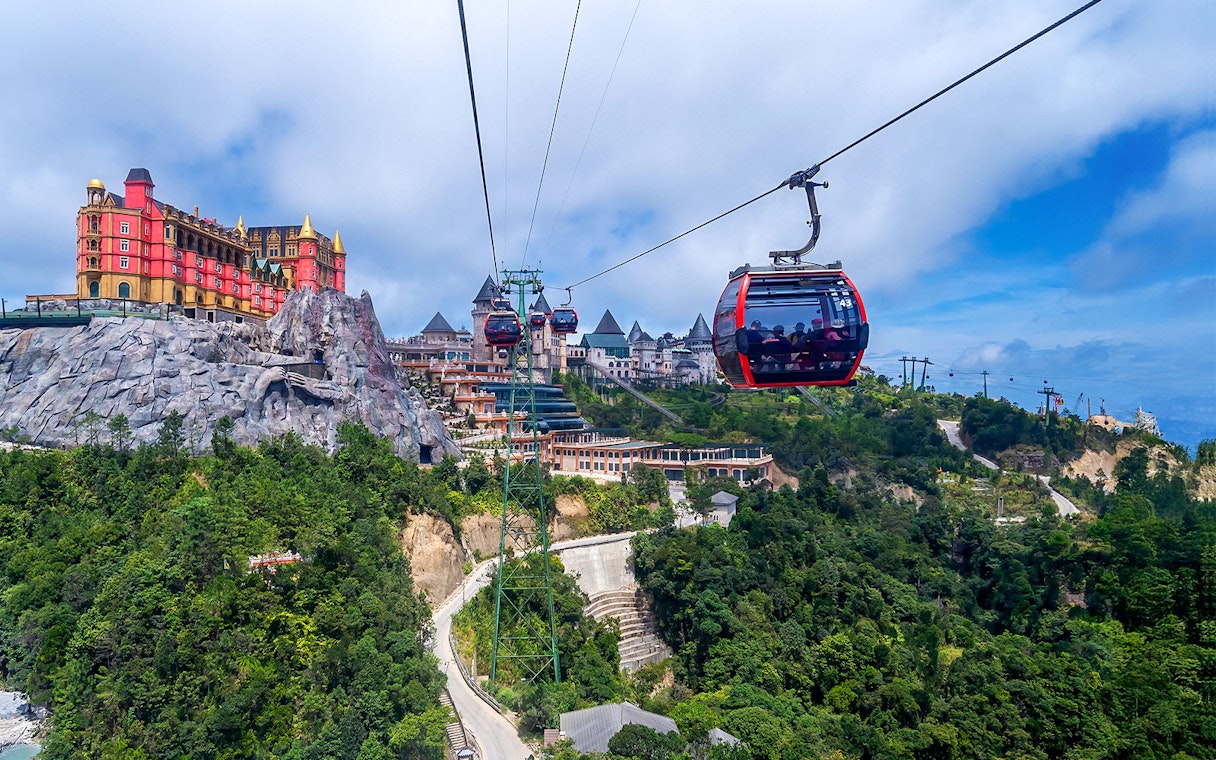 Cable car ascending to Ba Na Hills with scenic view of lush landscape and hilltop buildings.