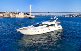 Luxury yacht cruising on the Bosphorus with Istanbul skyline and bridge in the background.
