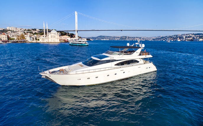 Luxury yacht cruising on the Bosphorus with Istanbul skyline and bridge in the background.