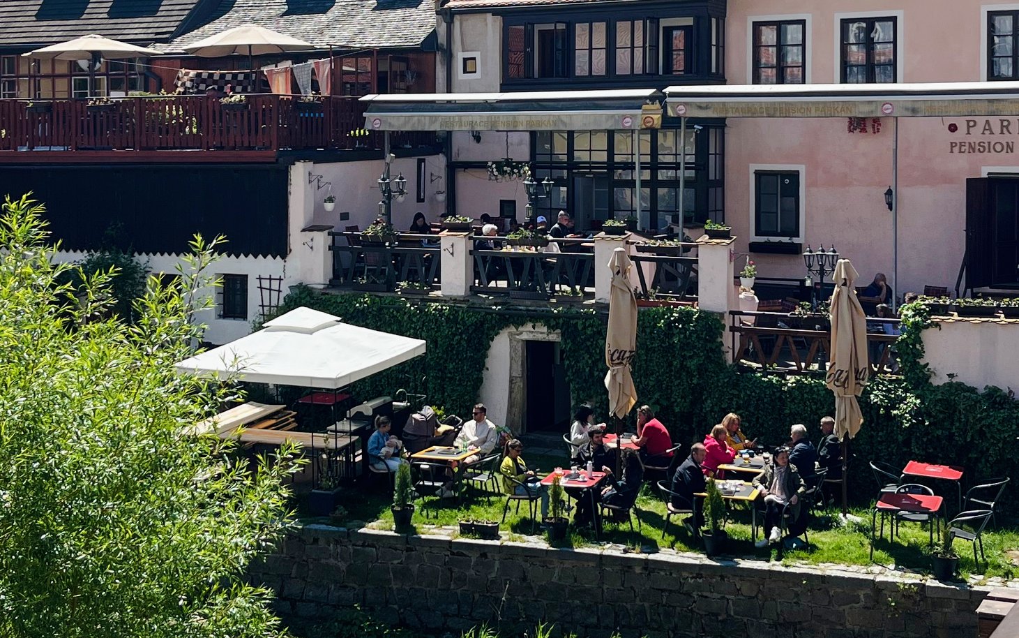 Outdoor dining area at a hotel in Český Krumlov with guests enjoying meals on a sunny day.