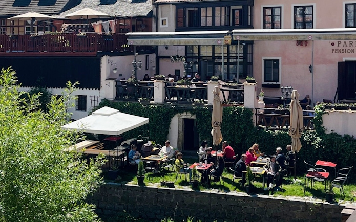 Outdoor dining area at a hotel in Český Krumlov with guests enjoying meals on a sunny day.
