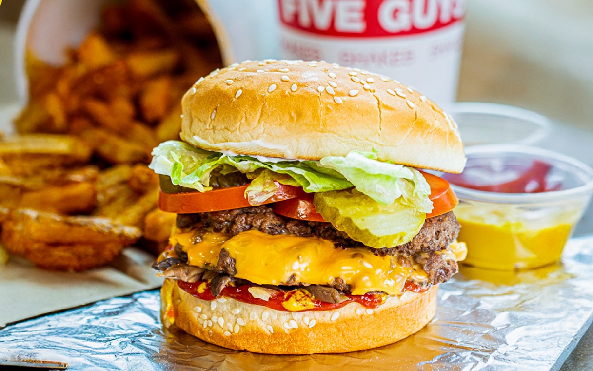 Burger with cheese, lettuce, tomato, and pickles, served with fries at Five Guys, Dubai Marina.